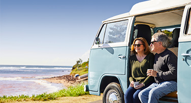 An older couple sitting in a Kombi van parked at a beach