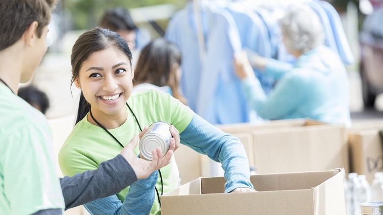 Male and female teenage food bank volunteers sort canned food items in cardboard boxes.
