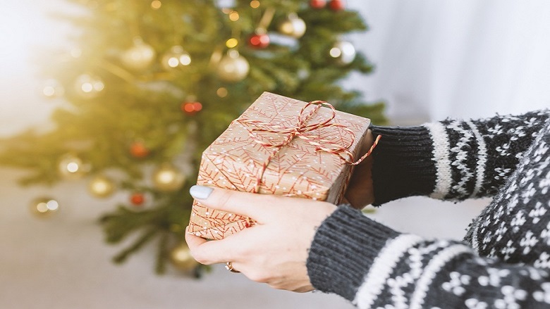 hands offering a present near a Christmas tree