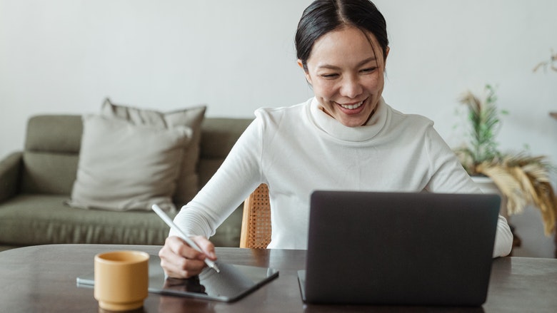 Woman on laptop and writing on tablet