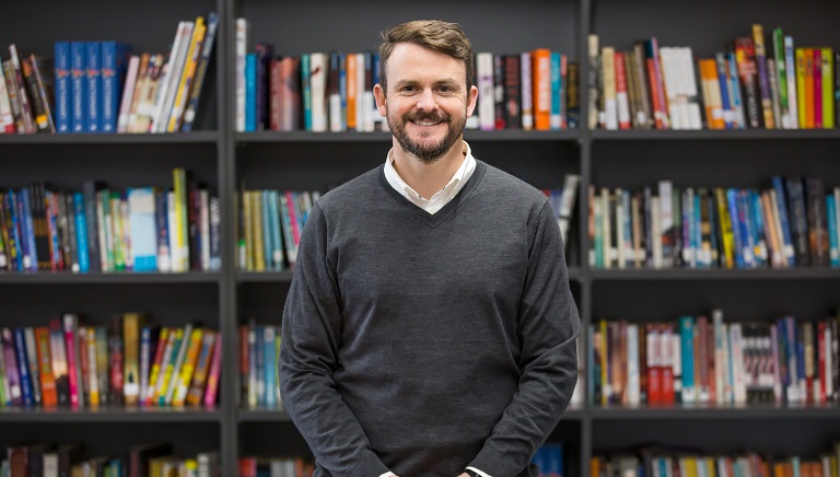Image of a man standing in front of a bookshelf 
