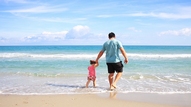 Dad and daughter paddle in the waves at the beach