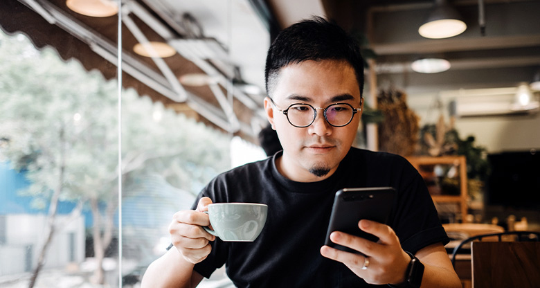 Man with coffee checking home loan on mobile phone