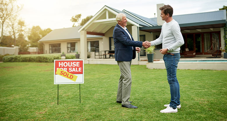 Buyer and agent in front of house with sold sign