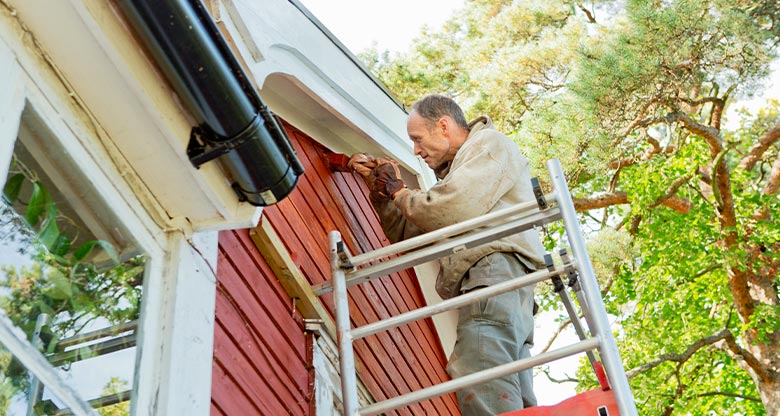 Man on ladder painting outside of house