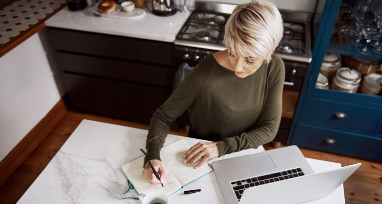 Image of a woman sitting at a kitchen bench working on laptop