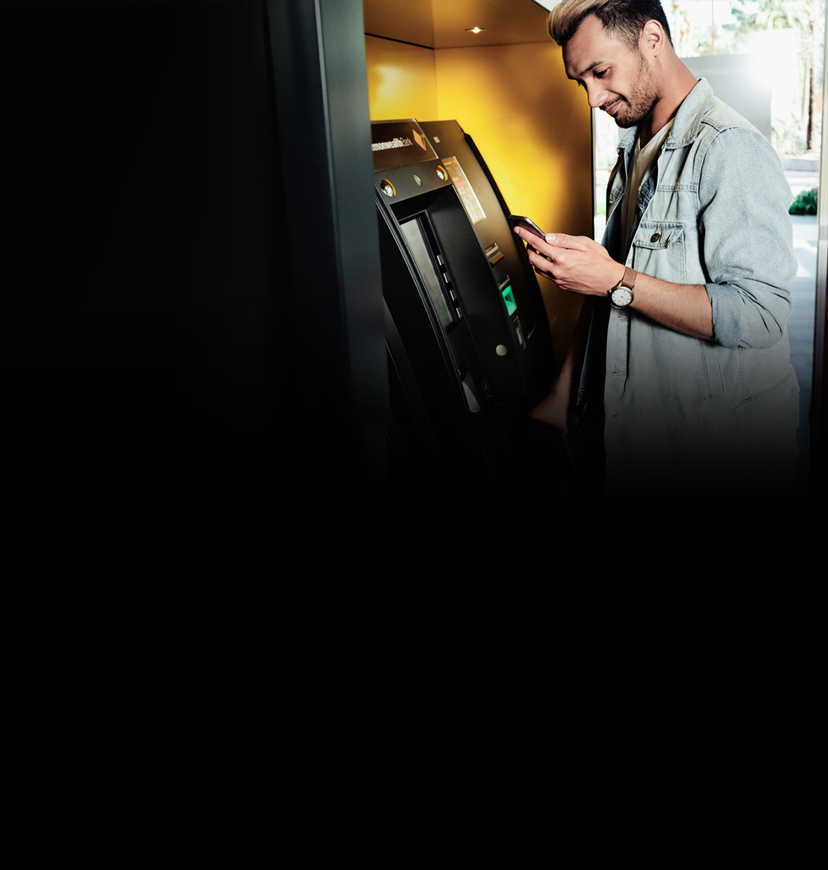 Image of person at a CommBank ATM, with mobile phone in hand