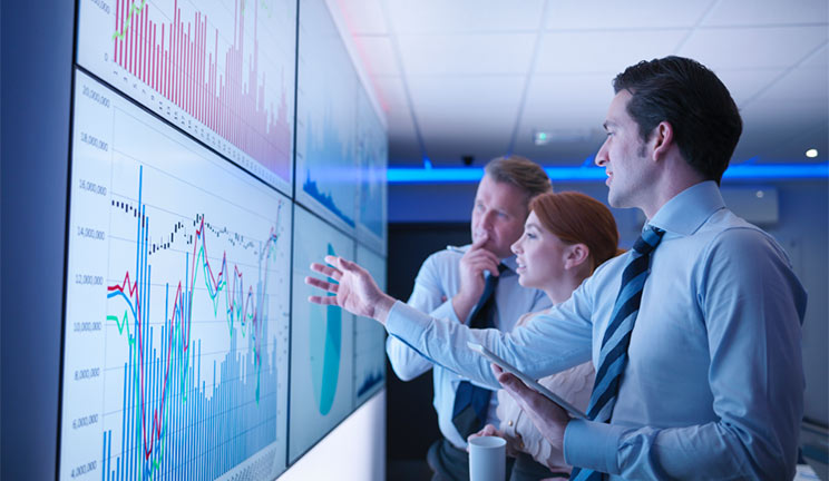 employees looking over graphs on large screen