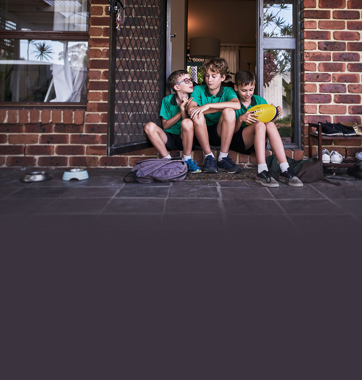 Three brothers sitting on the doorstep of their home after school