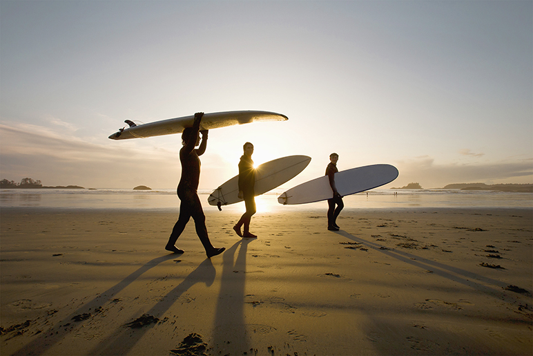 Image of three surfers walking along the beach at sunset