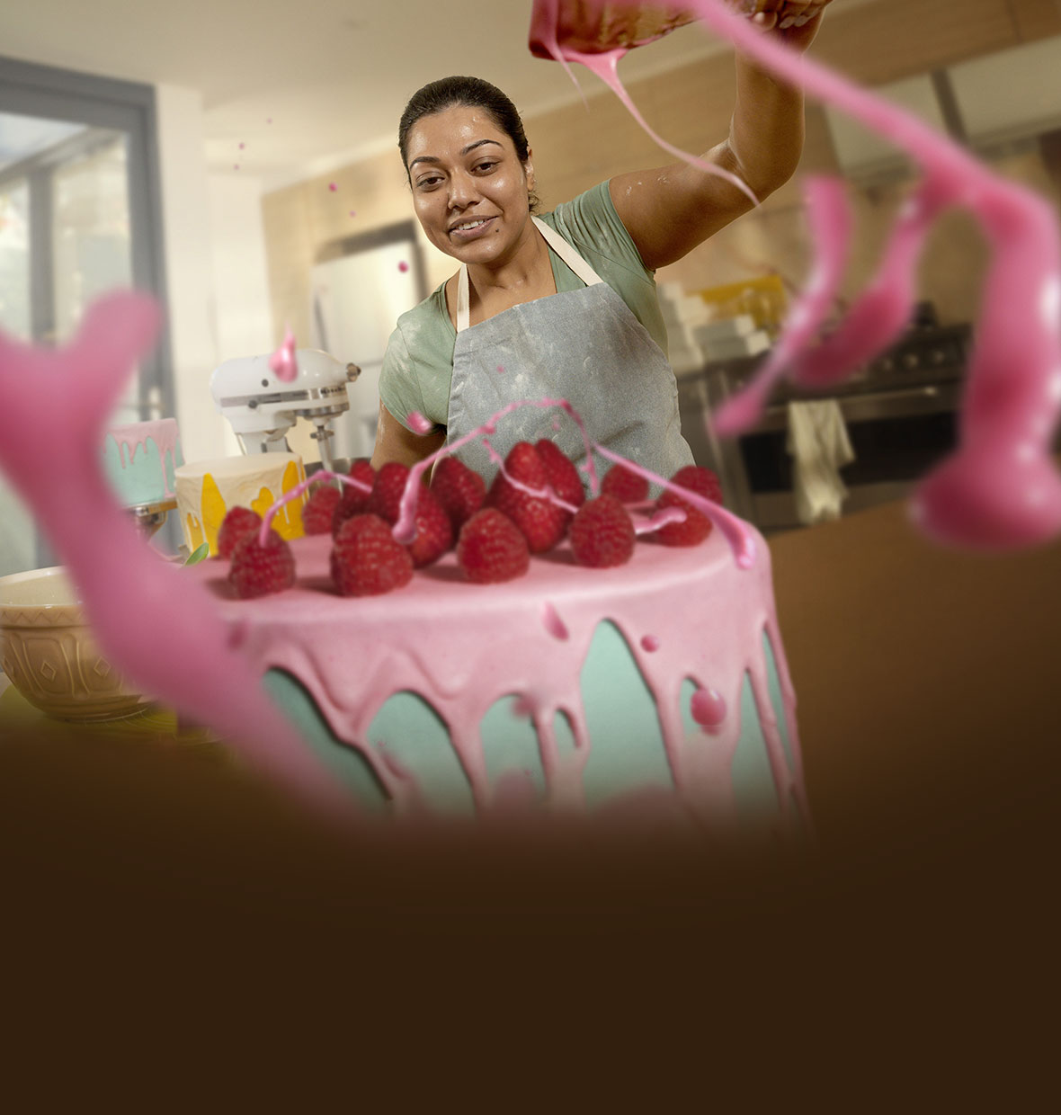 A woman flicks bright coloured icing onto a large cake topped with strawberries.